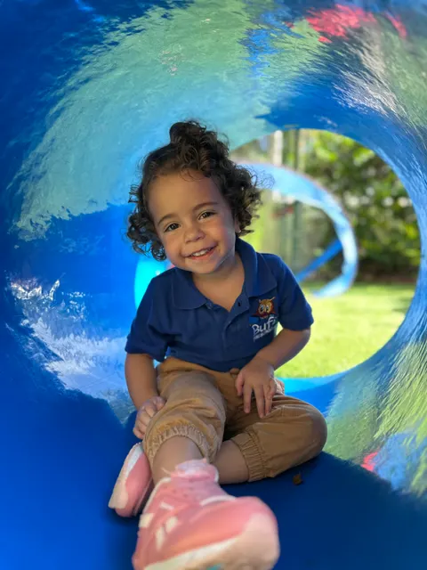 A toddler girl sitting inside a blue tunnel slide
