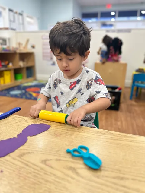 A boy rolling out playdough with a toy rolling pin