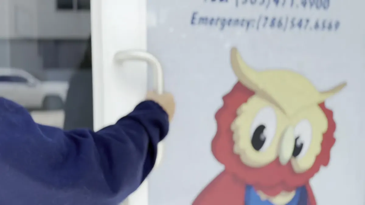 A child reaching for the front door at Bufi Preschool in Doral, FL, the owl mascot decal on the glass beside him