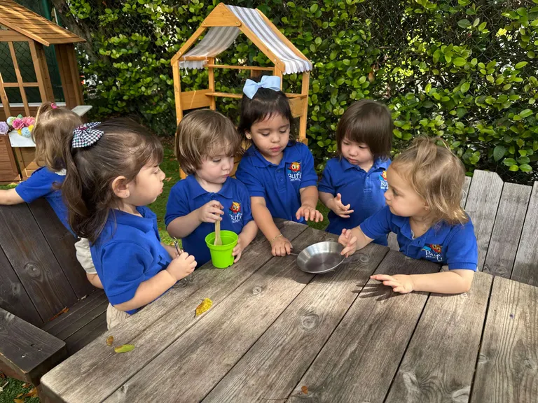 Niños explorando una bandeja sensorial en la mesa del patio