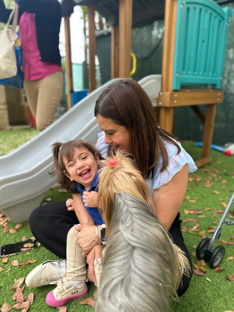 Una maestra arrodillada en el jardín abrazando a un niño que ríe